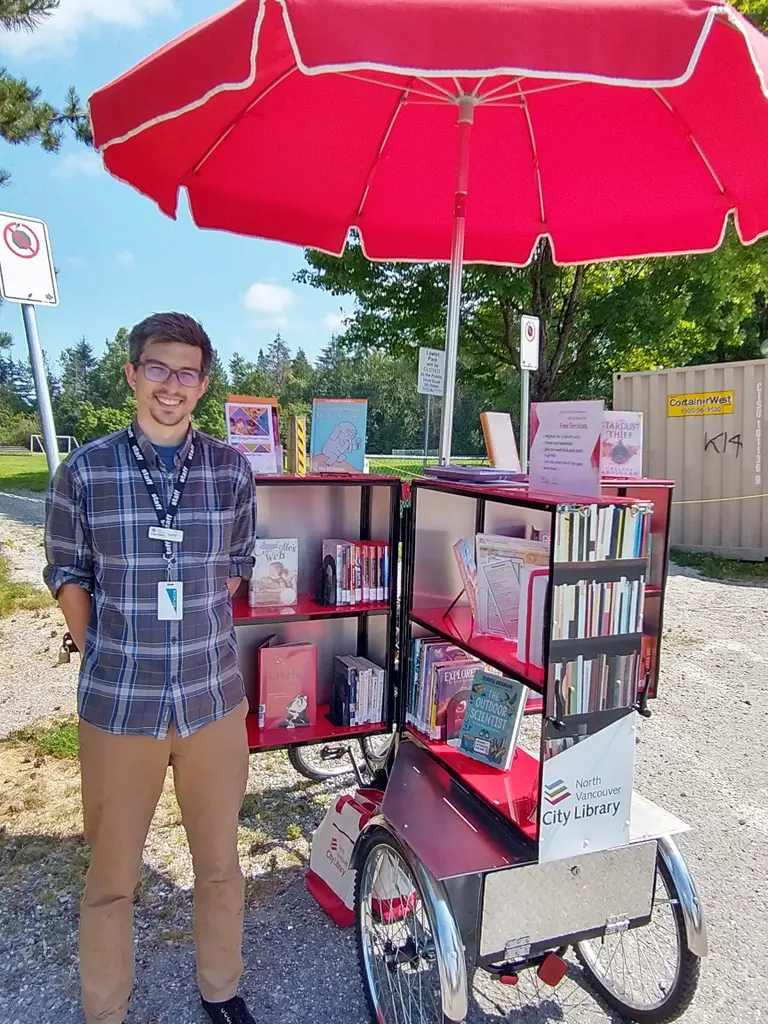 Kellen Malek standing next to the North Vancouver City Library book bike.